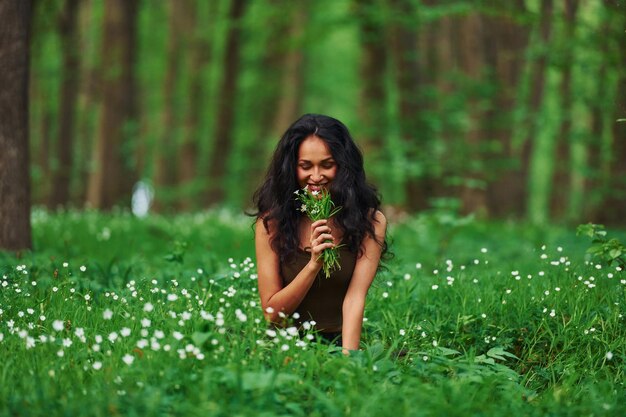 Bruna positiva in abiti casual seduti nella foresta durante il giorno