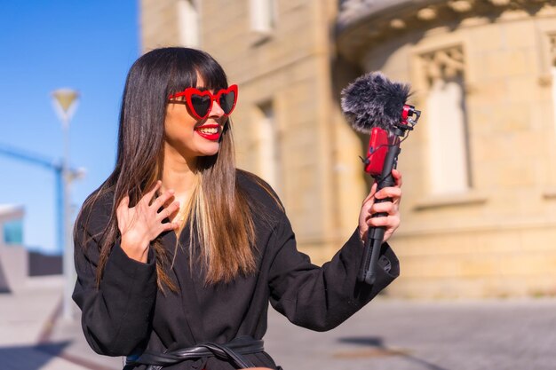 Bruna ragazza caucasica che fa un vlog il giorno di San Valentino occhiali da sole cuore rosso parlando al telefono e microfono