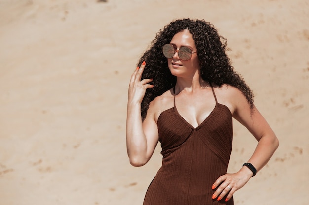 Bruna scura con voluminosi capelli ricci tra le sabbie in una duna di sabbia in un vestito volante