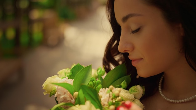 Bruna sposa in posa con fiori in giardino Donna che odora di fiori all'aperto