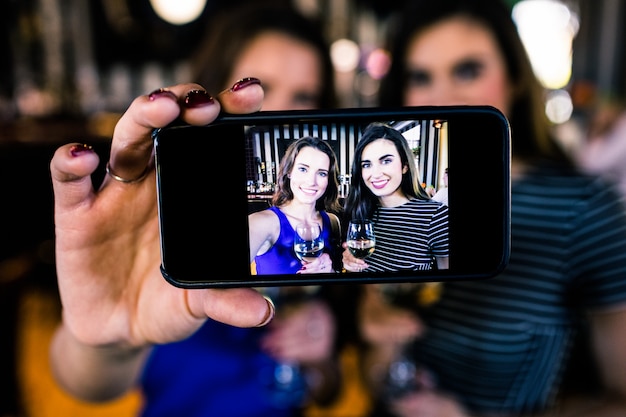 Brune felici che prendono selfie con vino bianco in una barra