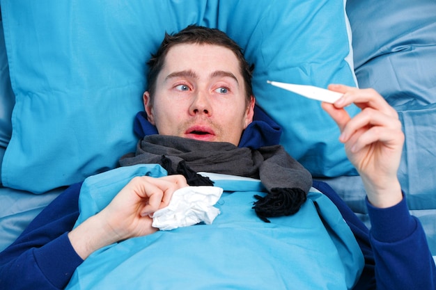 Brunet malato in sciarpa con termometro in mano sdraiato a letto