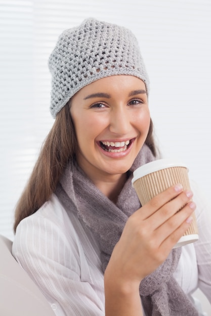 Brunette allegro con il cappello di inverno sulla tenuta della tazza di caffè