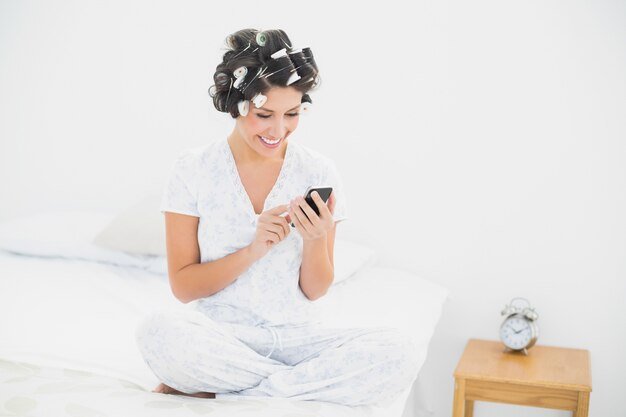 Brunette allegro in rulli dei capelli che inviano un testo sul letto