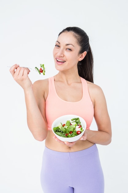 Brunette sorridente che mangia insalata