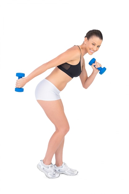 Brunette sportivo sorridente che risolve con i dumbbells