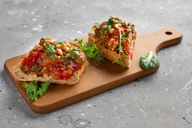 Bruschetta caponata con pinoli decorata con una foglia di basilico su una tavola di legno