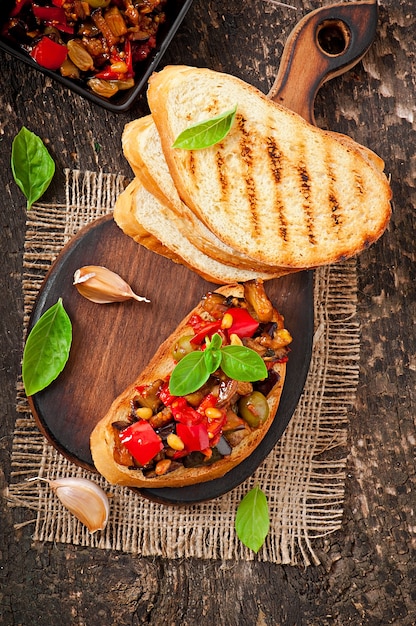 Bruschetta caponata con uvetta e pinoli decorata con una foglia di basilico