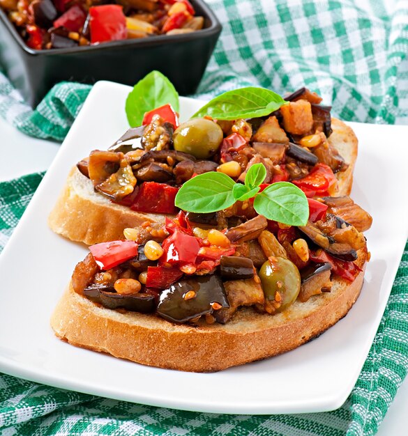 Bruschetta caponata con uvetta e pinoli decorata con una foglia di basilico