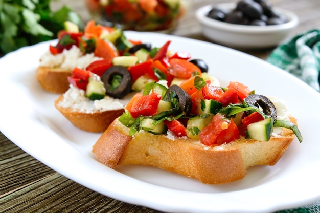 Bruschetta classica con pomodori e feta su un piatto bianco su un tavolo di legno. Panini italiani con baguette tostate, formaggio di capra, verdure fresche, basilico.