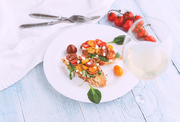 Bruschetta con formaggio, basilico, rucola e pomodorini e un bicchiere di vino bianco