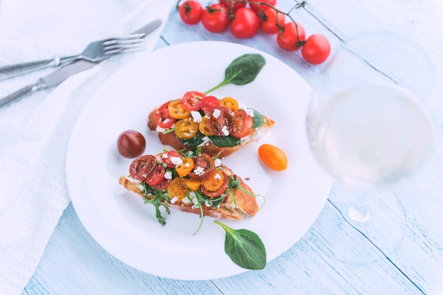 Bruschetta con formaggio, basilico, rucola e pomodorini e un bicchiere di vino bianco