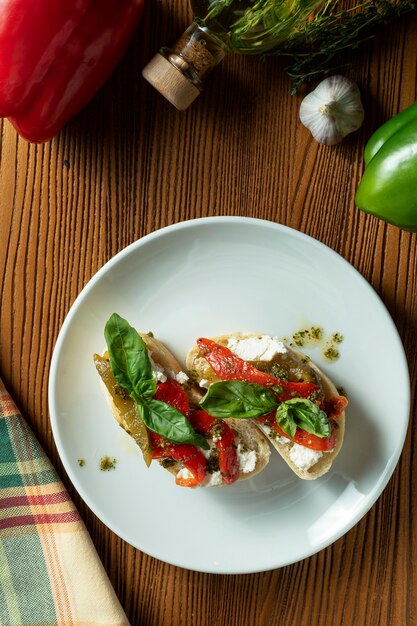 Bruschetta con peperone, basilico, salsa al pesto e mozzarella su un piatto bianco su un fondo di legno.