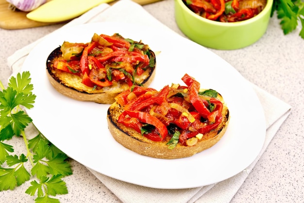 Bruschetta con pomodori arrostiti, peperoni, aglio, cipolle e prezzemolo in una ciotola su un tovagliolo su un tavolo di granito di sfondo