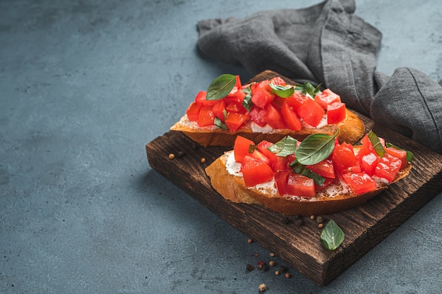 Bruschetta con pomodori e basilico su una tavola su uno sfondo scuro. Antipasto italiano. Vista laterale, spazio per la copia.