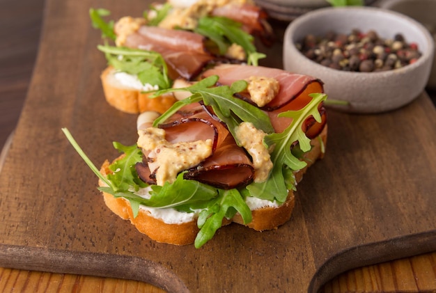 Bruschetta con prosciutto e rucola su una tavola di legno. Carne affumicata