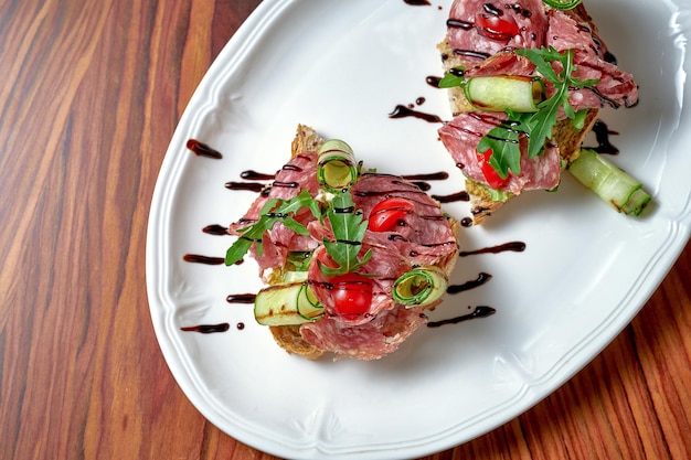 Bruschetta con salame e pomodori in un piatto bianco su fondo di legno