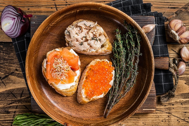 Bruschetta con salmone affumicato a caldo, caviale rosso ed erbe aromatiche. Fondo in legno. Vista dall'alto.