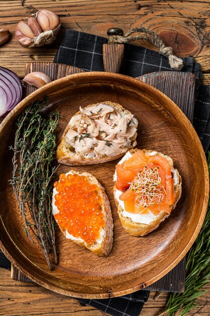 Bruschetta con salmone affumicato caldo, caviale rosso ed erbe aromatiche. Fondo in legno. Vista dall'alto.