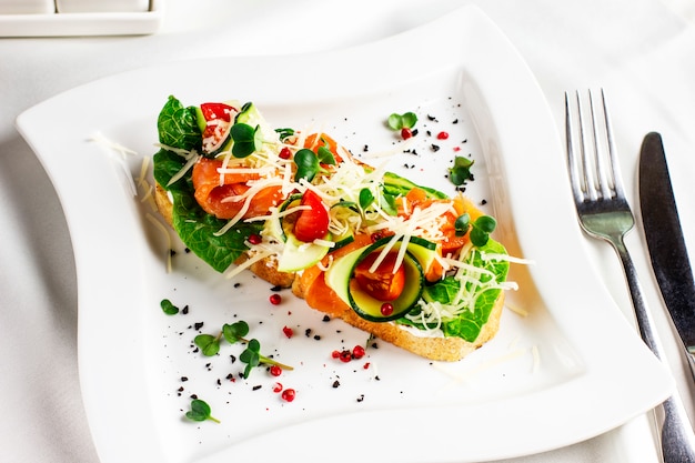 Bruschetta con salmone pesce rosso, verdure fresche ed erbe su un piatto bianco