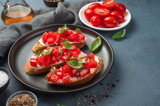 Bruschetta italiana con pomodoro, basilico e formaggio su sfondo grigio-blu. Vista laterale, spazio per la copia.