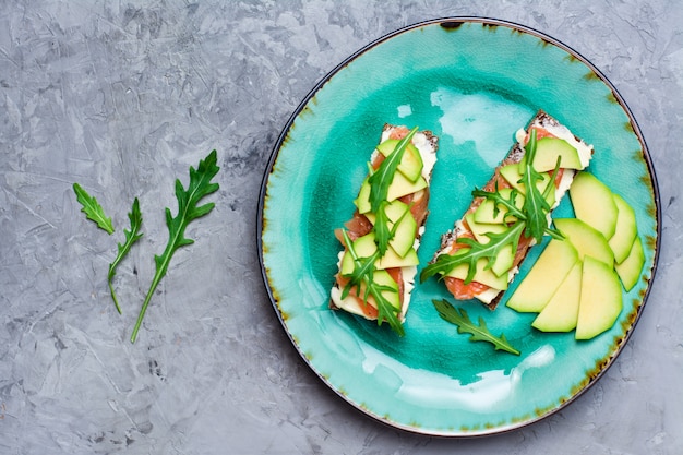 Bruschetta saporita con salmone, burro, avocado e rucola su un piatto