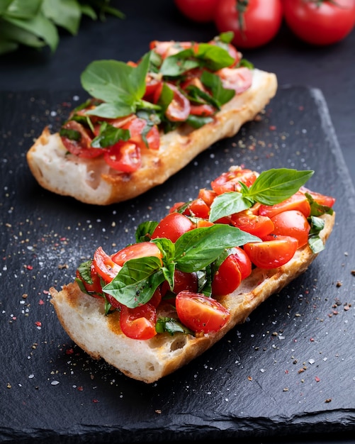 Bruschette fatte in casa con pomodorini e basilico closeup su una tavola di ardesia. Cucina italiana. Antipasti. Cibo vegano