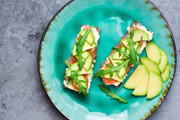 Bruschette pronte da mangiare con salmone, burro, avocado e rucola su un piatto