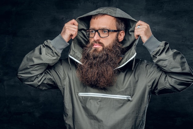 Brutale maschio hipster barbuto in un cappuccio su sfondo grigio.