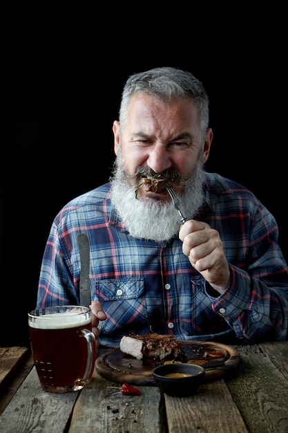 Brutale uomo adulto dai capelli grigi impazzito per la bistecca alla senape e birra, vacanze, festival, Oktoberfest o San Patrizio