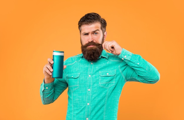 Brutale uomo barbuto tenere la bottiglia di balsamo per capelli che presenta articoli da toeletta tocco baffi