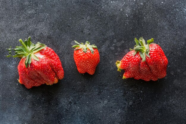 Brutta fragola organica matura tre su sfondo nero