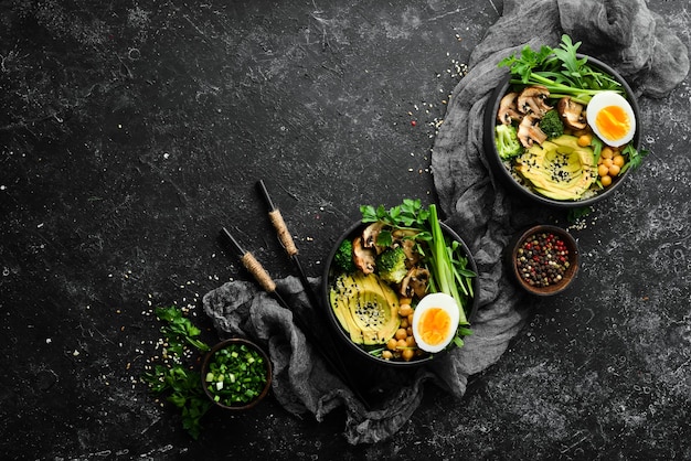 Buddha bowl avocado ceci funghi uova e rucola in una ciotola nera Vista dall'alto Spazio libero per il testo