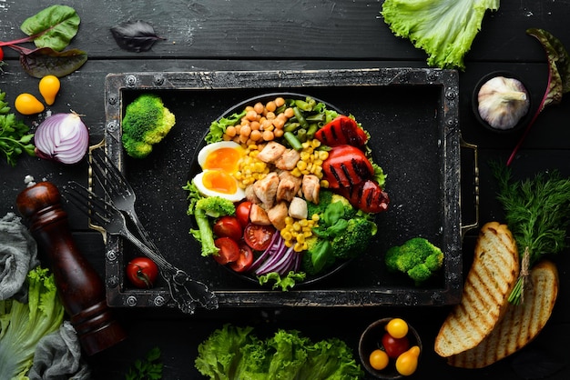 Buddha Bowl pollo ceci broccoli pomodori uovo paprika cipolla in un piatto nero su sfondo nero Vista dall'alto Spazio libero per il testo