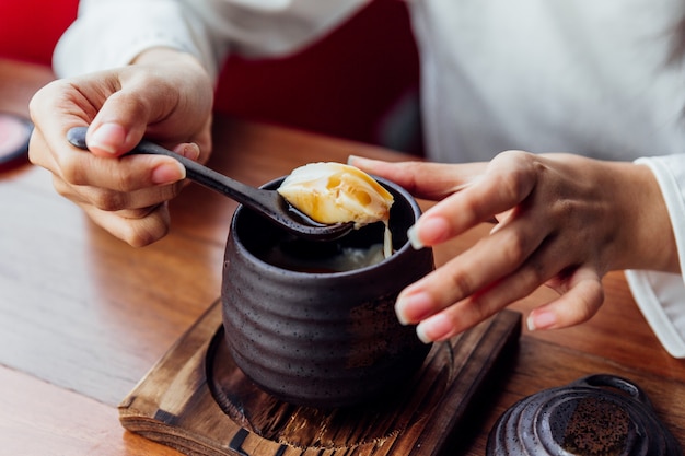 Budino al caramello giapponese servito in tazza di ceramica nera che raccoglie budino morbido a mano donna