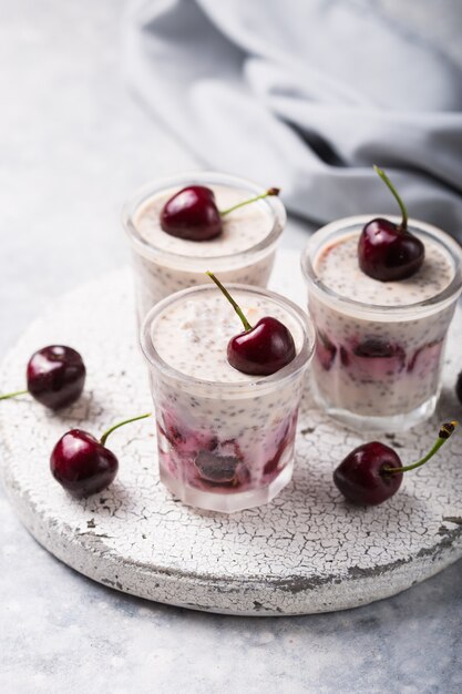 Budino di Chia con bacche di ciliegia, yogurt naturale, in un bicchiere su una superficie grigia