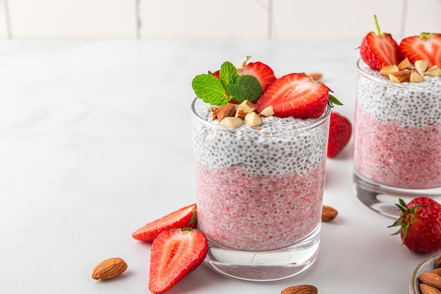 Budino di Chia in bicchieri con fragole fresche, mandorle e menta su superficie bianca per colazione vegana