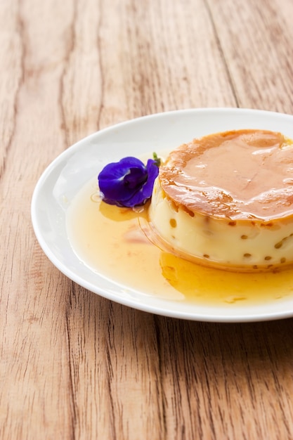 Budino di crema di caramello fatto in casa sul piatto bianco. Sopra il tavolo di legno.