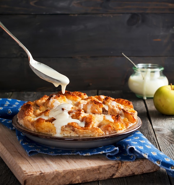 Budino di pane. Casseruola tradizionale inglese per la colazione con mele e salsa alla vaniglia. Budino di pane e burro su fondo di legno vecchio. Messa a fuoco selettiva.