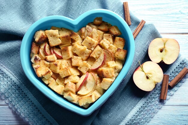 Budino di pane delizioso con mele in ciotola a forma di cuore sul tovagliolo