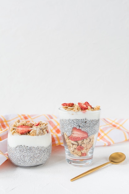 Budino di semi di chia durante la notte con latte di mandorle, yogurt, muesli fatto in casa, fragole secche e mandorle in due bicchieri e cucchiaio. Concetto di superfood e cibo vegano. Copia spazio, messa a fuoco selettiva