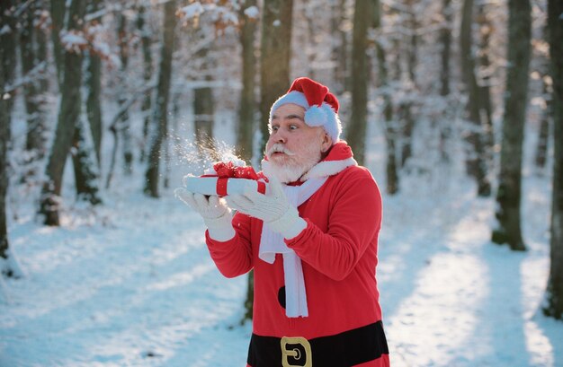 Buffo Babbo Natale soffiare la neve sul regalo di Natale fuori