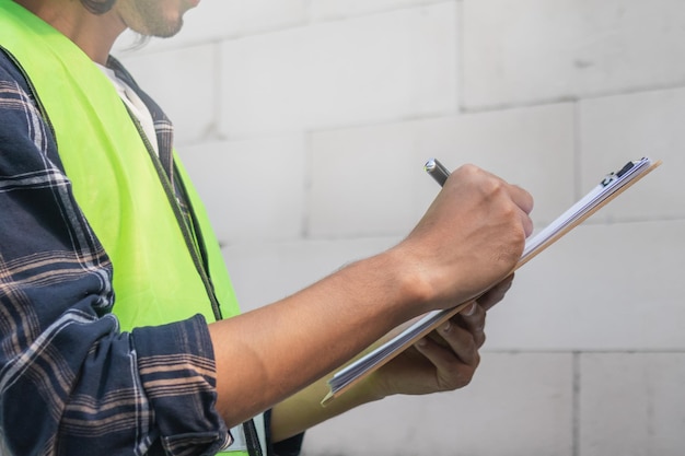 Builder lavoratore asiatico giovane appaltatore uomo che tiene appunti per pianificare ang indossando il casco per la sicurezza ispezionare il ricostruito per la costruzione e la ristrutturazione casa controllare il difetto in loco