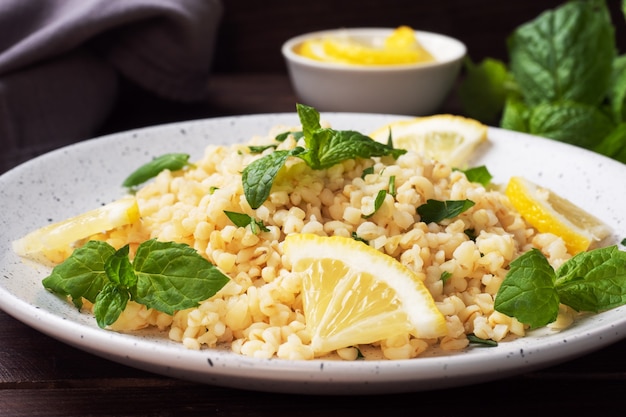 Bulgur bollito con limone fresco e menta su un piatto. Un piatto tradizionale orientale chiamato Tabouleh. fondo in legno scuro.