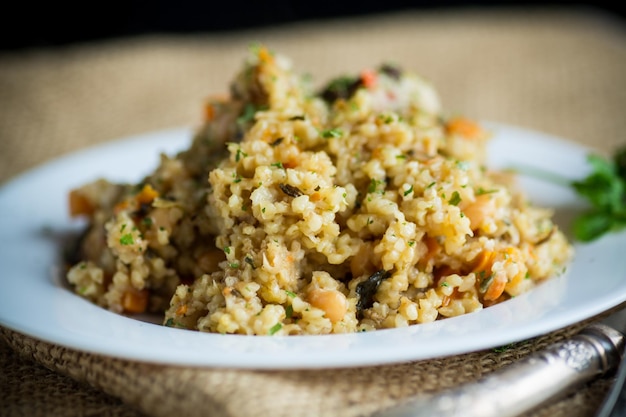 bulgur cotto con verdure, carote e funghi secchi in un piatto su un tavolo di legno