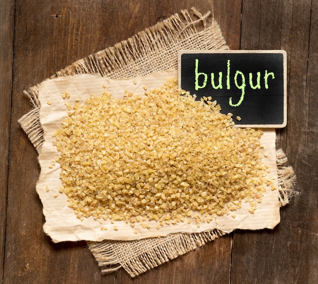 Bulgur organico crudo con una lavagna su una vista di legno del piano d'appoggio