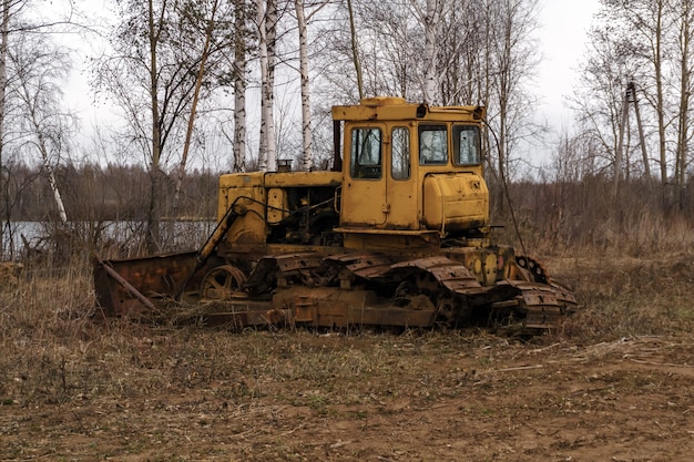 Bulldozer arrugginito rotto con tracce strappate si trova in un boschetto di primavera vicino al lago