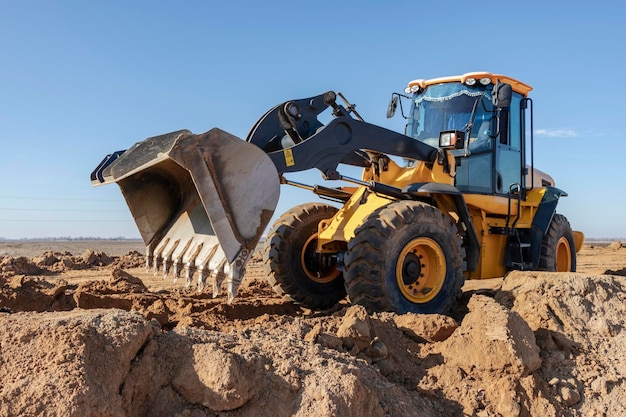 Bulldozer o caricatore sposta la terra in cantiere contro il cielo blu Una macchina movimento terra sta livellando il sito Costruzione di attrezzature pesanti per lavori di sterro