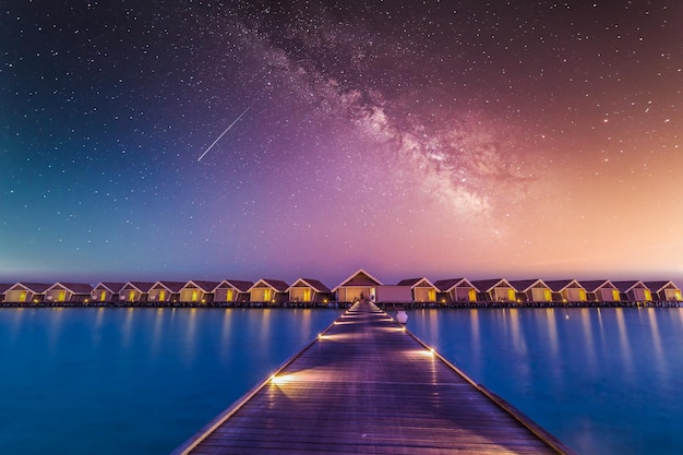 Bungalow e ville sull'acqua di notte, paesaggio tropicale. Viaggi di lusso alle isole Maldive, via lattea