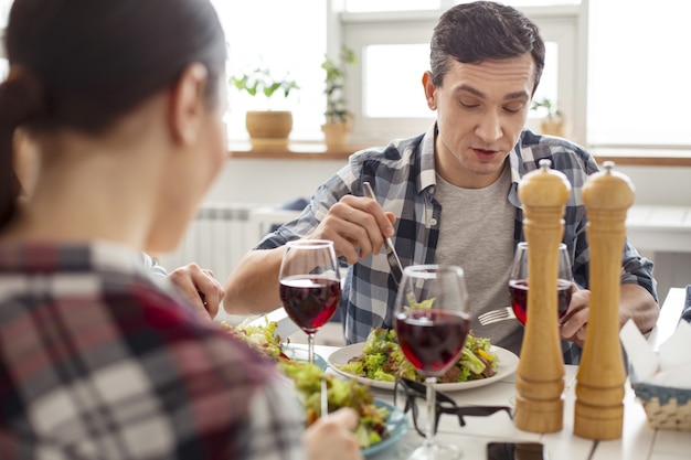 Buon appetito. Uomo dai capelli scuri concentrato bello mangiare un'insalata e parlare e rilassarsi con i suoi amici